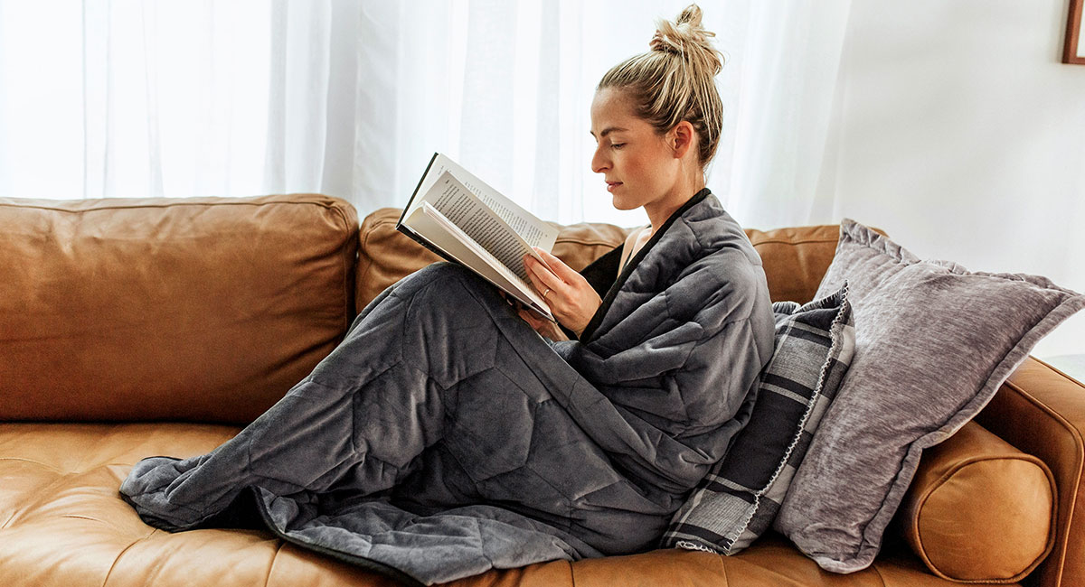 Woman reading a book wrapped up in a weighted blanket